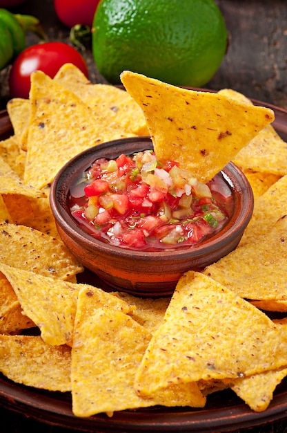 Mexican nacho chips and salsa dip in  bowl on wooden