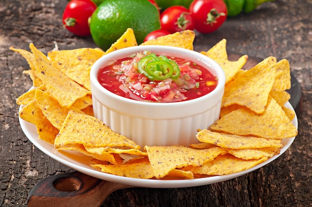 Mexican nacho chips and salsa dip in bowl on wooden