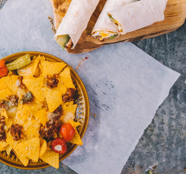 Free photo mexican nachos chips in plate with mexican tacos on cutting board over paper