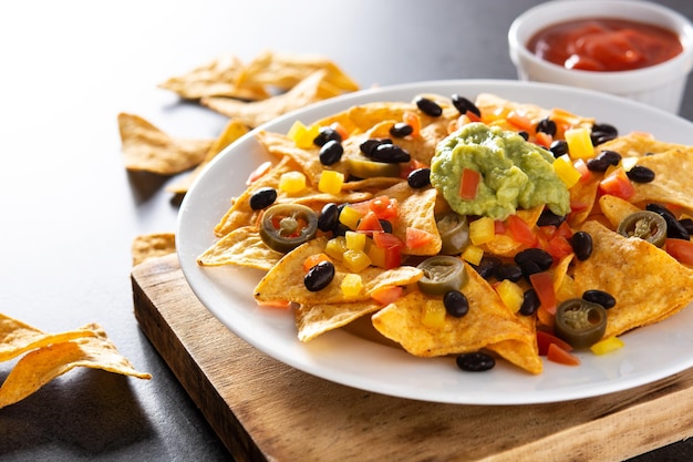 Free Photo mexican nachos tortilla chips with black beans, guacamole, tomato and jalapeno on black background