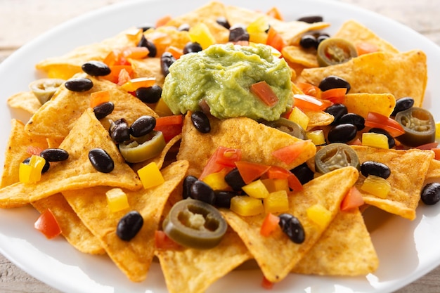 Free Photo mexican nachos tortilla chips with black beans, guacamole, tomato and jalapeno on wooden table