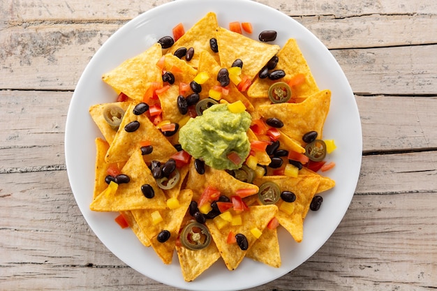 Free Photo mexican nachos tortilla chips with black beans, guacamole, tomato and jalapeno on wooden table