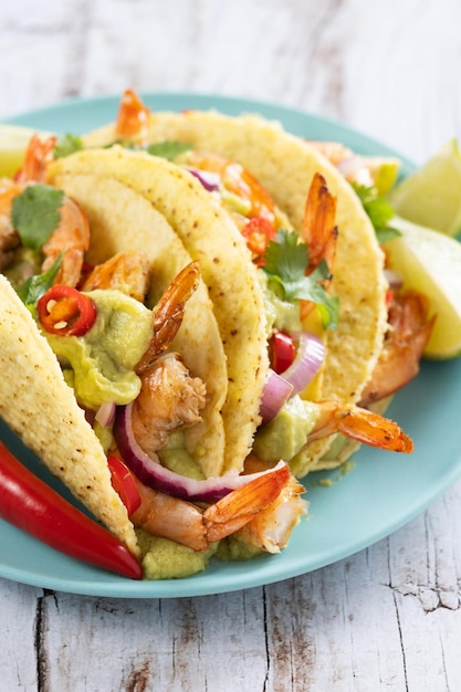 Free photo mexican tacos with shrimpguacamole and vegetables on wooden table