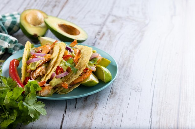 Mexican tacos with shrimpguacamole and vegetables on wooden table