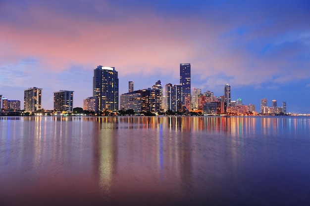 Miami city skyline panorama at dusk with urban skyscrapers over sea with reflection