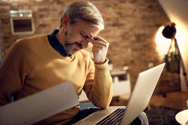 Mid adult businessman having a headache while working late at home