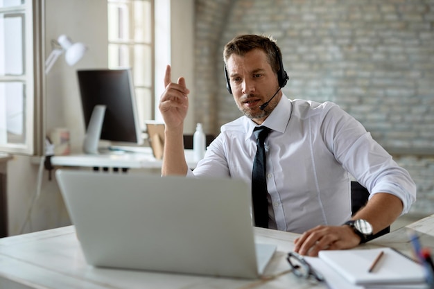 Free Photo mid adult businessman wearing headphones while having video call over laptop in the office