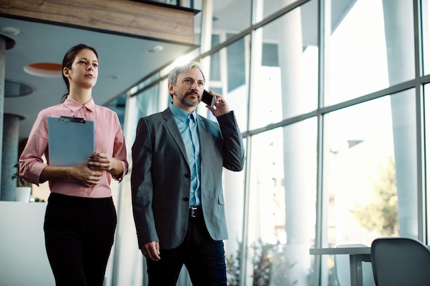 Free Photo mid adult ceo talking on the phone while walking through a hallway with female colleague