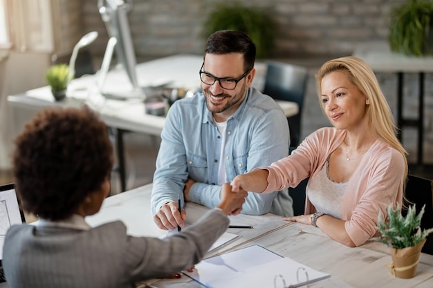 Mid adult couple reaching an agreement with real estate agent in the office Women are handshaking