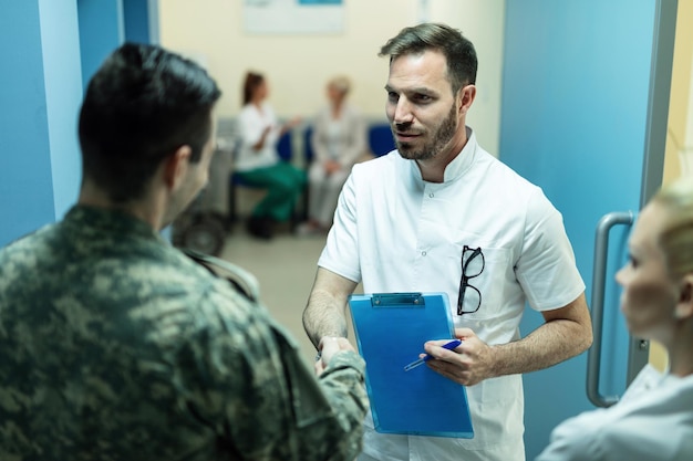 Free Photo mid adult doctor and military officer shaking hands while standing in a hallway at the hospital