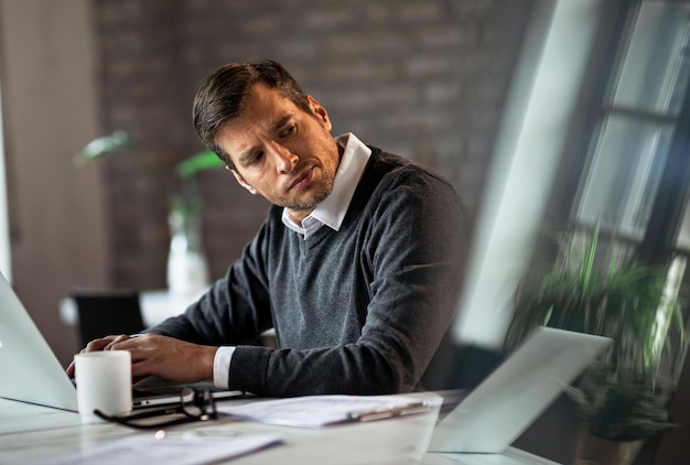 Mid adult entrepreneur working on a computer and looking away while feeling dissatisfied about something