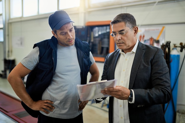 Mid adult manager and car mechanic analyzing data while going trough reports in auto repair shop