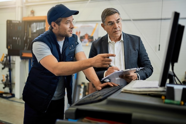 Free photo mid adult manager and car mechanic talking while using computer in auto repair shop