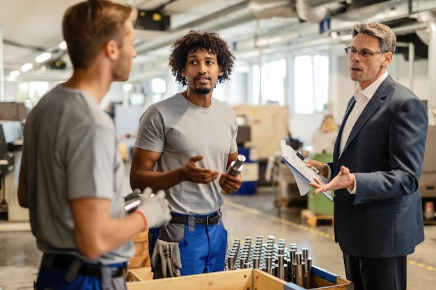 Free Photo mid adult manager discussing with metal workers while performing quality control check of manufactured rod cylinders in a factory