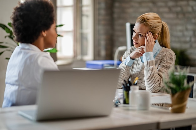 Free photo mid adult woman feeling worried while talking to african american doctor during medical appointment