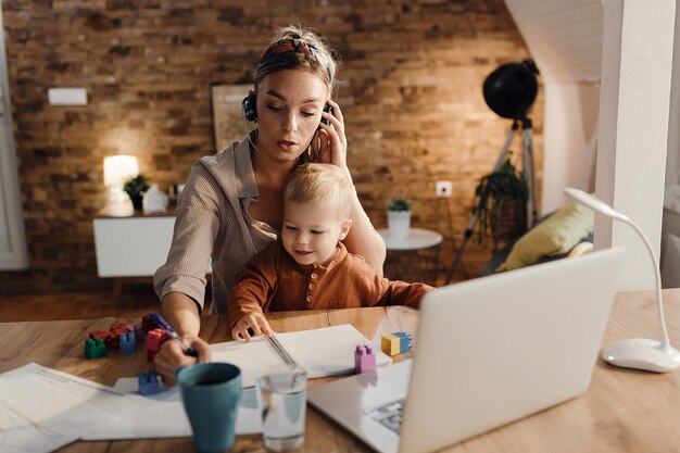 Mid adult working mother taking notes during conference call at home