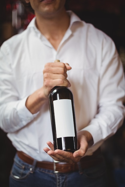 Mid section of bar tender holding a bottle of wine