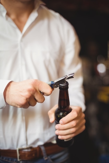 Mid section of bartender opening a beer bottle