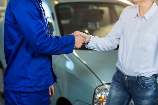 Mid-section of customer shaking hands with mechanic