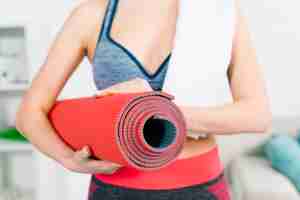 Free photo mid section of fitness young woman holding red exercise mat