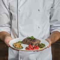 Free photo mid section of male chef holding prepared beef steak with vegetables