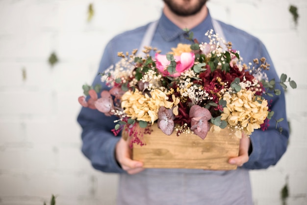 Mid section of man holding wooden crate with colorful flowers