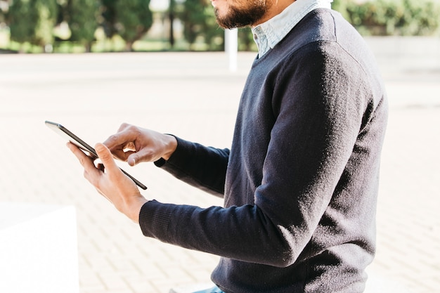 Mid section of a man sitting in the park using touch screen mobile phone