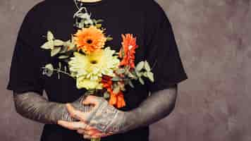 Free photo mid section of a man with tattoo in his hand holding gerbera bouquet