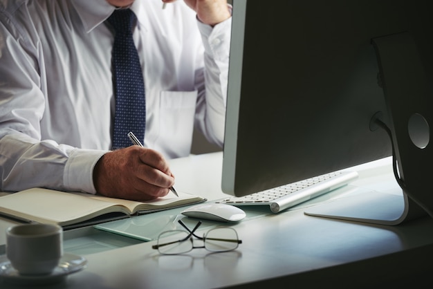 Free photo mid section of unrecognizable man in formalwear making notes at workplace computer