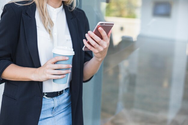 Mid section of woman holding disposal coffee cup holding smartphone