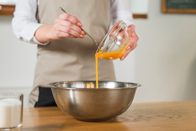 Free Photo mid section of woman pouring the egg yolk in the stainless steel bowl on wooden table