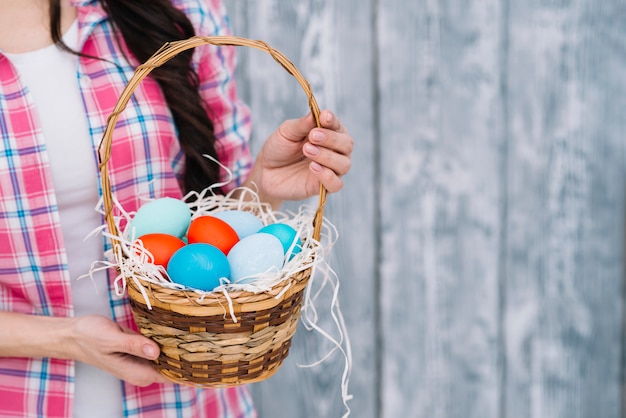 Mid section of woman's hand holding colorful easter eggs in the basket against blurred background