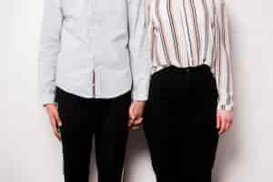 Free photo mid section of young couple holding each other's hand standing against white wall