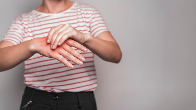 Mid section of young woman having pain in hand against gray background