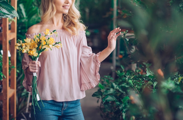 Mid section of a young woman holding yellow flower bouquet in plant nursery