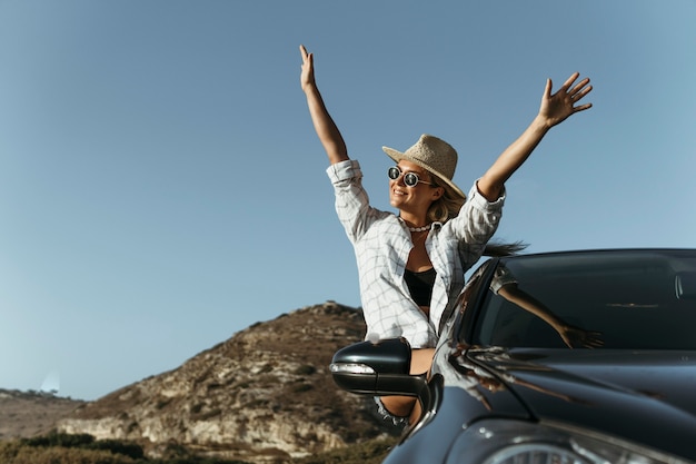 Mid shot blonde woman out of car window with hands in the air