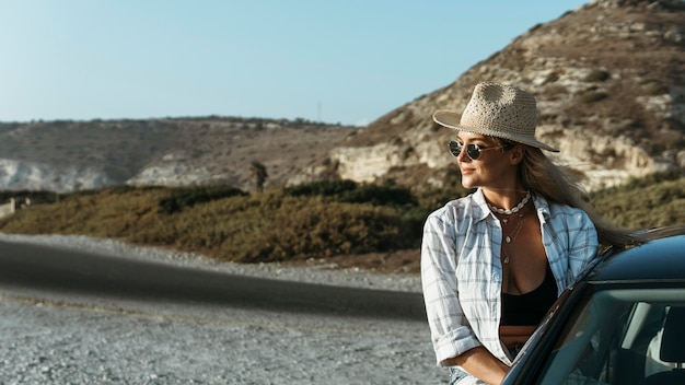 Free photo mid shot blonde woman standing out of car window on beach