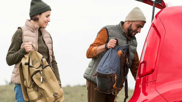 Free photo mid shot couple putting backpacks in trunk