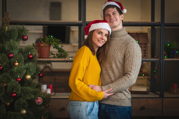 Mid shot couple wearing santa hats embracing eachother