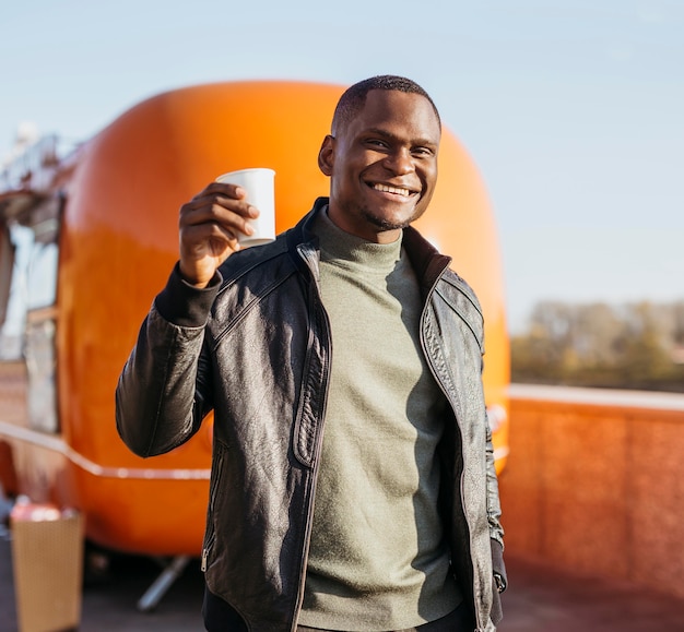 Mid shot happy man holding coffee cup in front of food truck