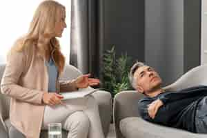 Free photo mid shot man laying on couch in therapy cabinet near woman counselor