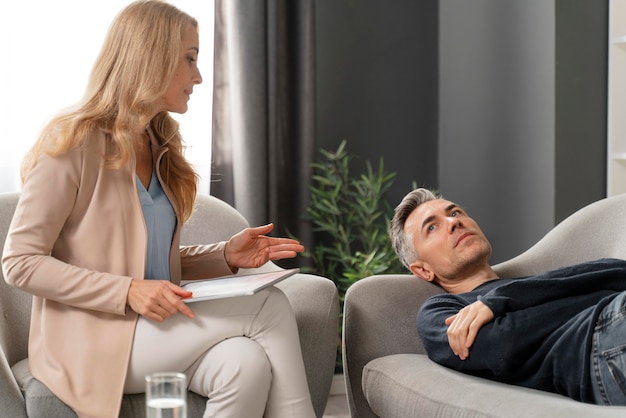 Mid shot man laying on couch in therapy cabinet near woman counselor