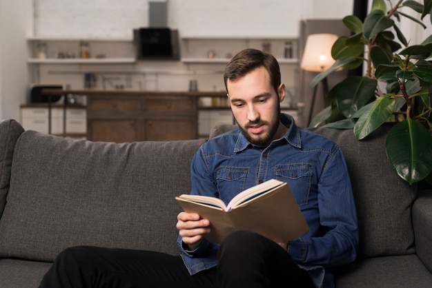 Mid shot man sitting on couch and reading book