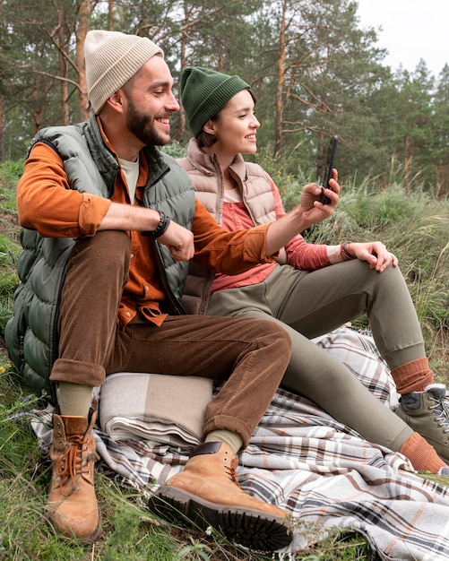 Mid shot man sitting on grass and taking photos with phone near girlfriend