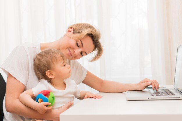 Mid shot mother holding baby staying at desk and smiling