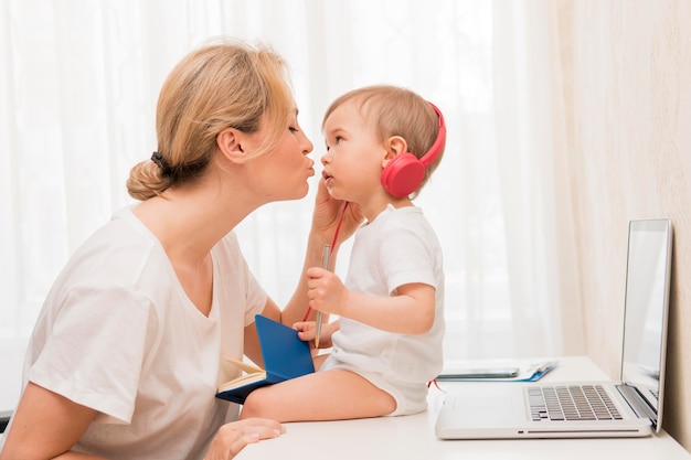 Mid shot mother kissing baby on desk with headphones