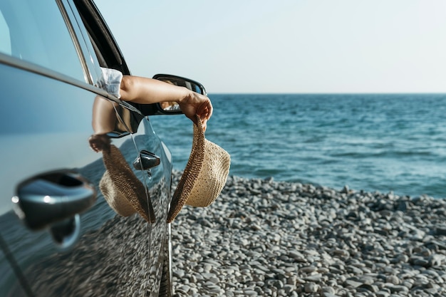 Free photo mid shot woman hand hanging out of car window and holding hat near sea