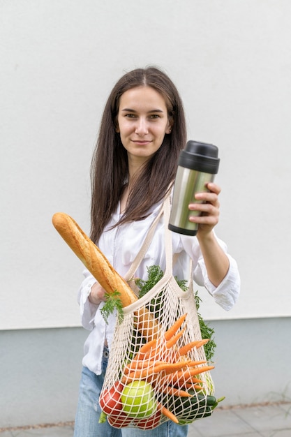 Free photo mid shot woman holding thermos and reusable bag