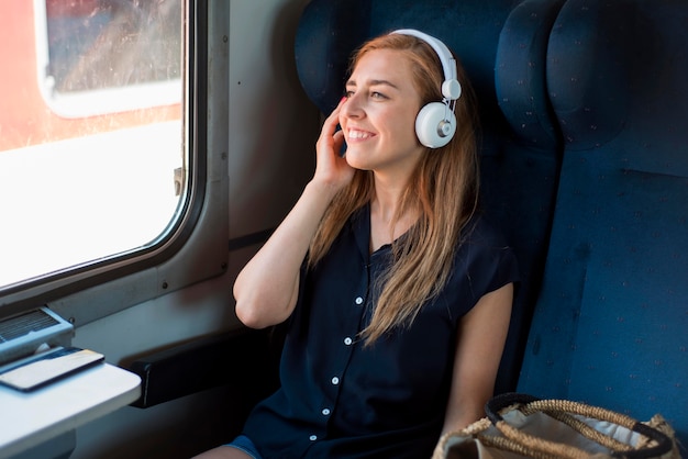 Mid shot woman sitting in train listening to music