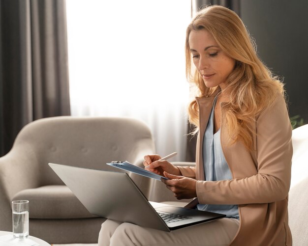 Mid shot woman therapist taking notes with laptop on lap